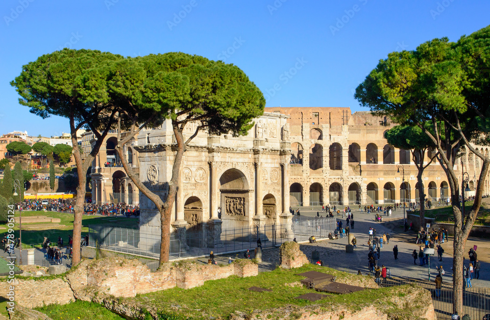 Blue sky, green grass, stone pines, Triumphal arch of Constantine and Colosseum in Rome, Italy