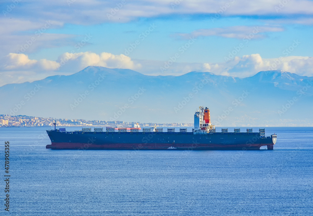 Big cargo ship in the Gulf of Naples, city coastline, mountains and blue sky with clouds