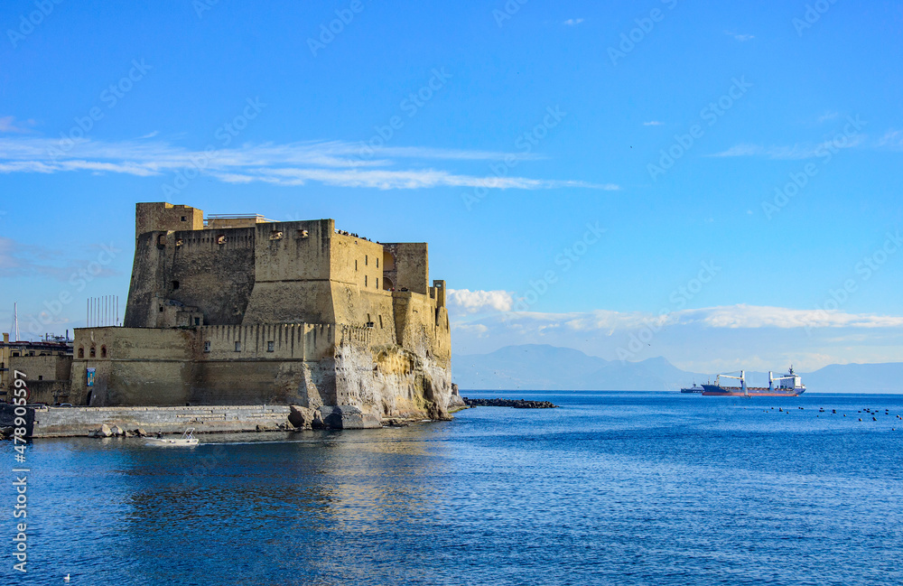 Cargo ship and sea view with Castel dell'Ovo (Egg Castle), a seafront castle in Naples, on the former island (now a peninsula) of Megaride, on the Gulf of Naples in Campania, Italy.