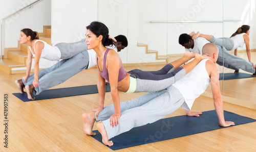 Sporty adult concentrated females and males doing stretching workout in pairs during group training at gym