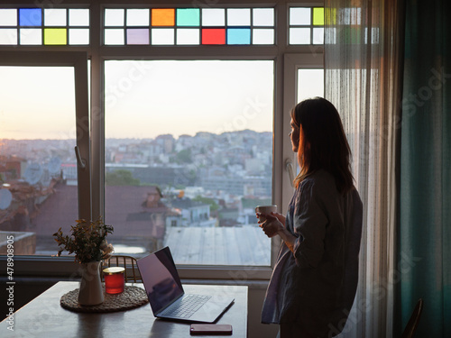 Woman with a coffee looking to the window at evening