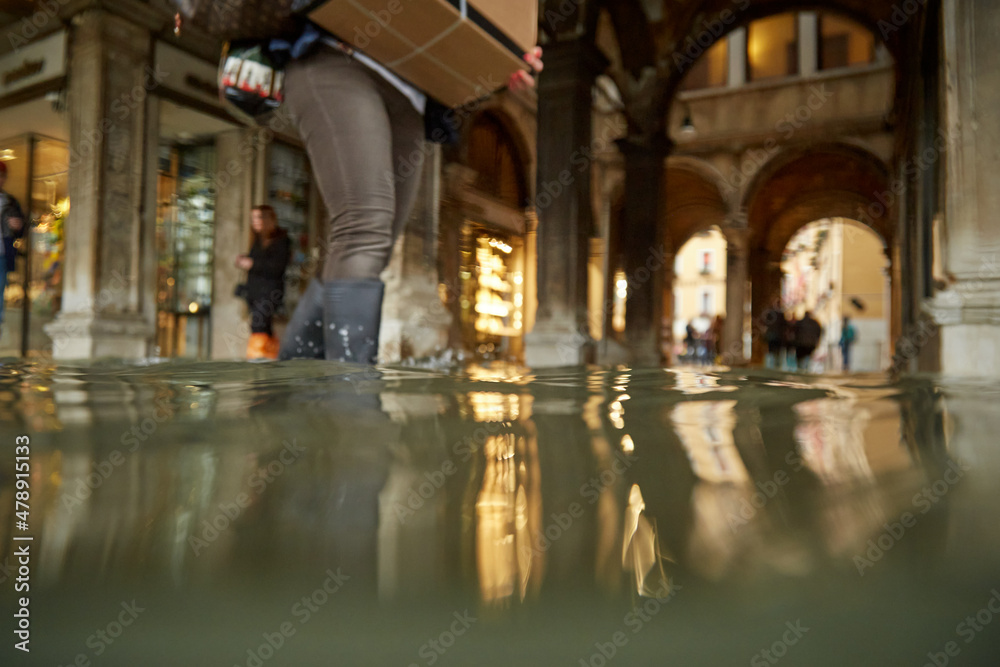 Venice floods, king tide, gumboot shopper wades with parcel Venice floods, king tide, gumboot shopper wades with parcel