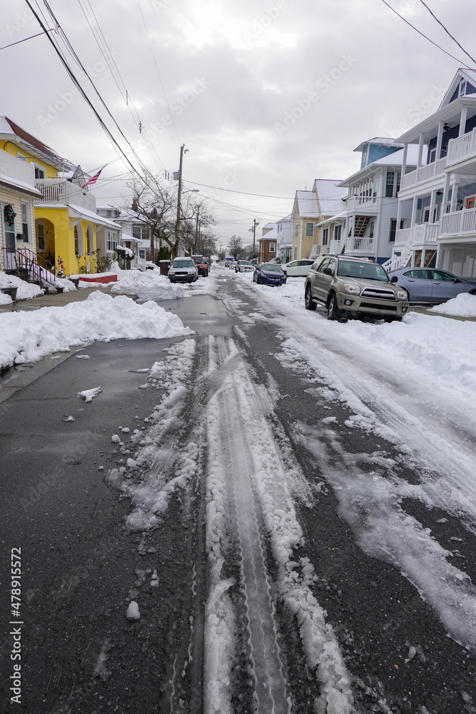 Small one way snow covered street with the center partially plowed and cars parked on both sides in deep snow Small one way snow covered street with the center partially plowed and cars parked on both sides in deep snow