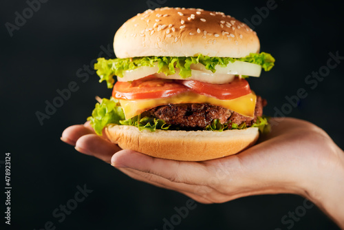 Tasty burger sandwich in hand isolated on black background