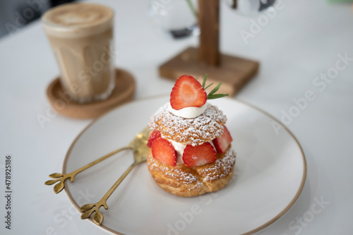 Fresh choux cream puff with whipped cream and strawberries on white plate.