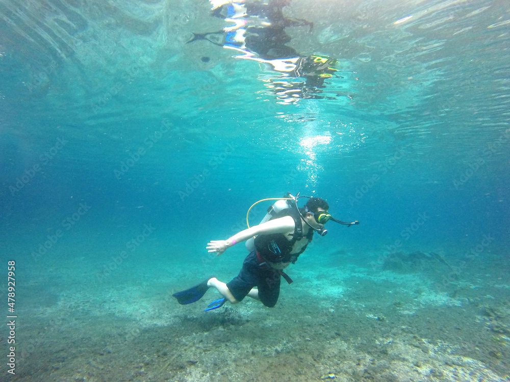 Latino adult man dives underwater with scuba equipment oxygen tank, visor, fins, enjoys sports and entertainment activity
