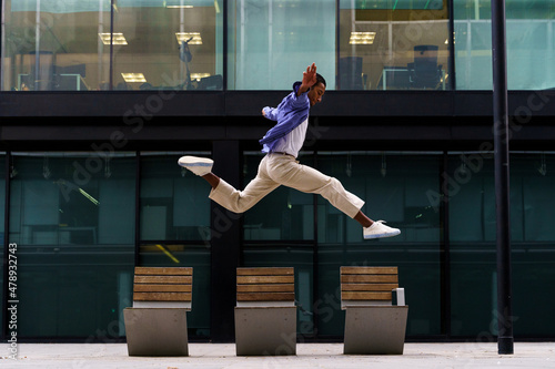 Stylish man dacing and jumping over street bench