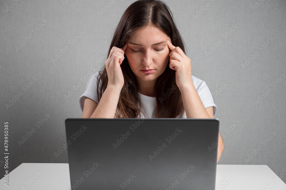 young woman massaging temples while sitting in front of laptop. young woman massaging temples while sitting in front of laptop.
