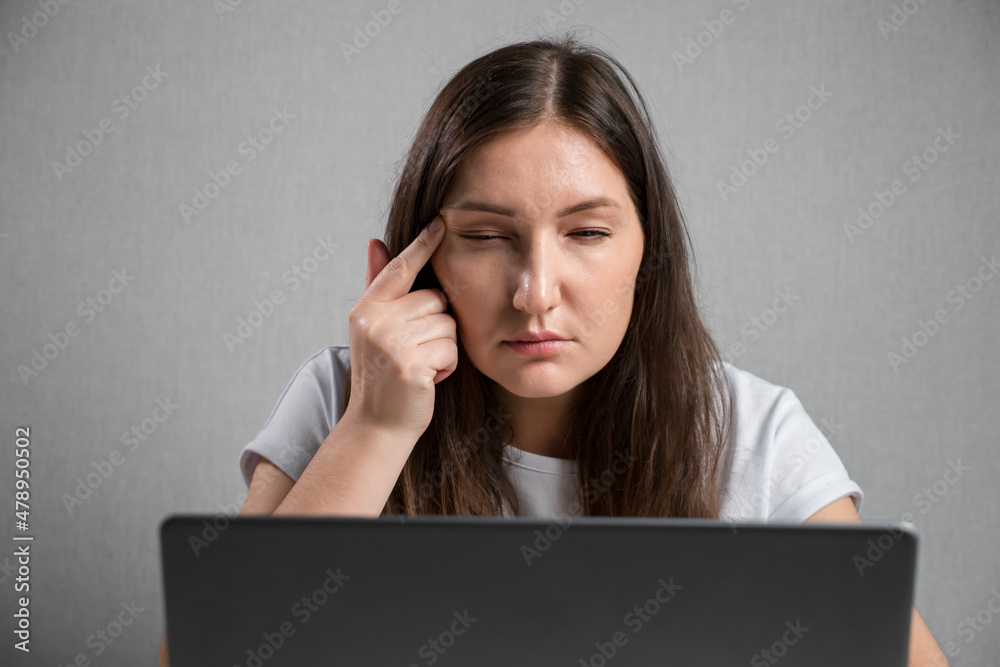 young brunette woman sitting at the laptop squints eyes. young brunette woman sitting at the laptop squints eyes.