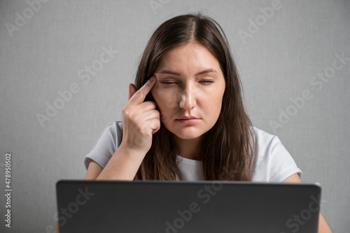 young brunette woman sitting at the laptop squints eyes. photo