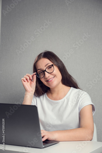 young brunette woman in glasses sitting in front of a laptop and smiling, copy space.