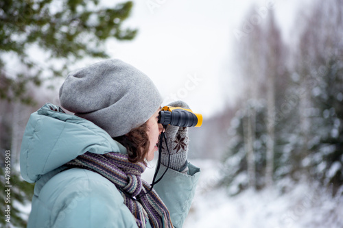 young woman in winter forest with yellow binoculars. Walking in the wild. Observation of nature in the winter season. Travel concept