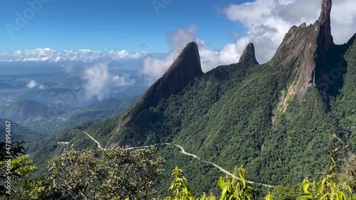Panning movement showing meandering road beneath the Finger of God peak among Brazilian mountain range called Serra dos Orgaos in Teresopolis with city Rio de Janeiro below in the distance photo