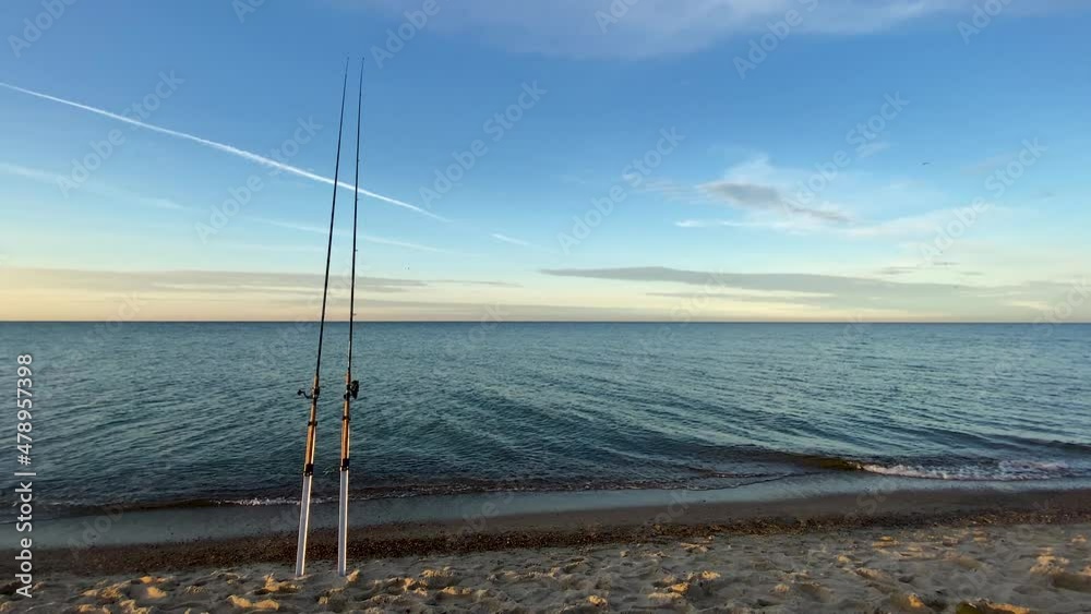 Two Fishing Rods Standing On The Sand With Seascape In Background. wide Two Fishing Rods Standing On The Sand With Seascape In Background. wide