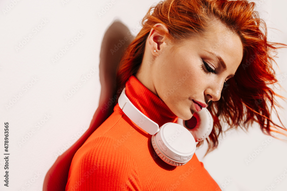Stylish ginger woman leaning against a white wall Stylish ginger woman leaning against a white wall