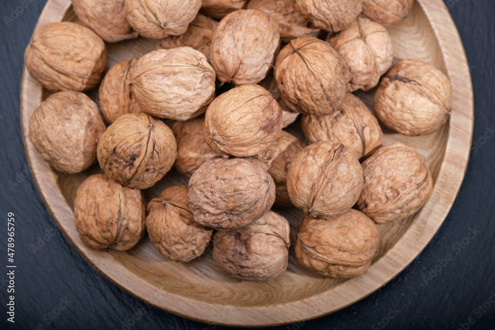 Group of walnuts on a black background. Nuts on a wooden plate close-up. Walnut on black top view copy space. Group of walnuts on a black background. Nuts on a wooden plate close-up. Walnut on black top view copy space.