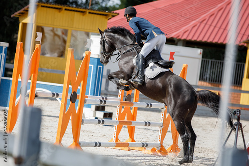 closeup portrait of black stallion horse and handsome man rider jumping obstacle during showjumping competition in summer