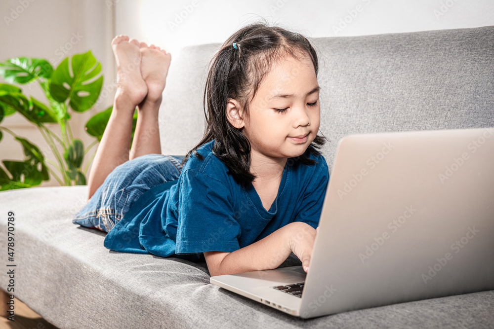 Cheerful Little kid girl studying online class with laptop and headphones at home. A New normal, Covid-19 coronavirus. Social Distance learning education technology gaming and homeschooling concept Cheerful Little kid girl studying online class with laptop and headphones at home. A New normal, Covid-19 coronavirus. Social Distance learning education technology gaming and homeschooling concept