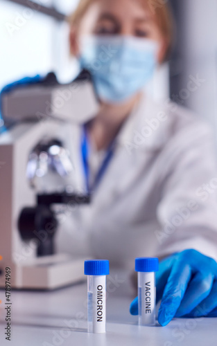 Fototapeta Naklejka Na Ścianę i Meble -  Female Lab Worker Wearing PPE Researching Covid-19 Omicron Variant And Vaccine With Microscope