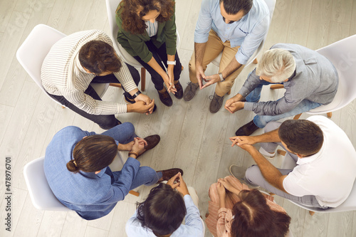 Overhead view of young and mature patients meeting for conversation with psychologist or psychotherapist. High angle shot of group of people sitting in circle during therapy session with psychiatrist