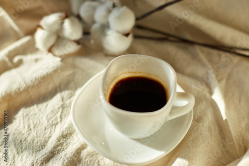 Cup of coffee in bed with cotton flowers   morning mood  Organic and natural linen cotton textile bedclothes  copy space.