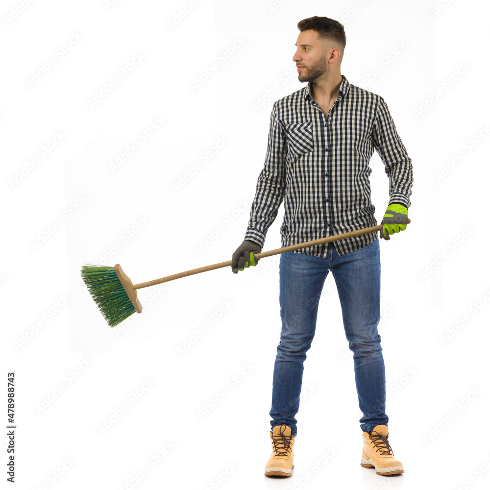 Handsome young man is standing with broom and looking to the side. Full length, isolated. Handsome young man is standing with broom and looking to the side. Full length, isolated.