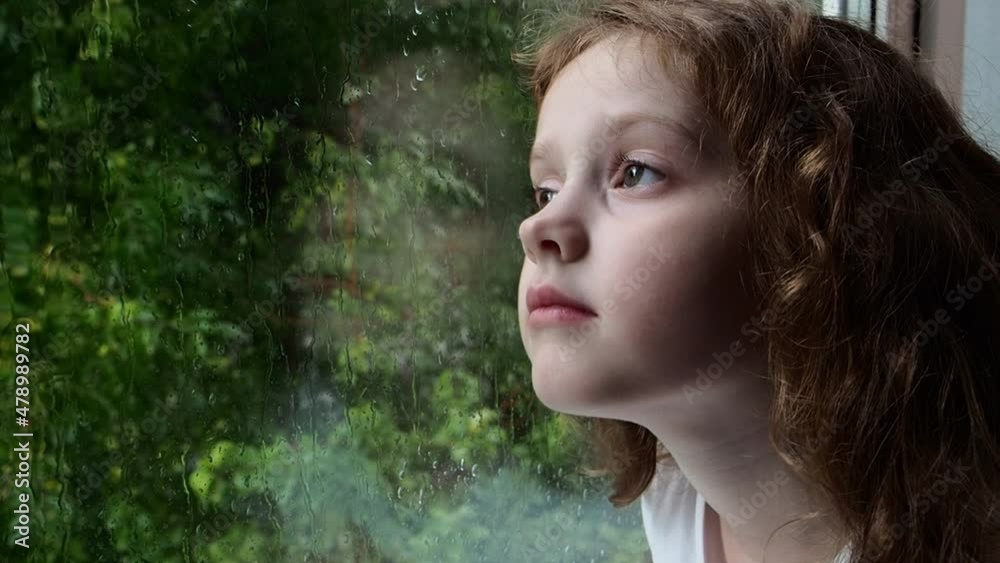 Sad little girl looking out the window on rain drops through wet glass autumn bad weather. Sad little girl looking out the window on rain drops through wet glass autumn bad weather.