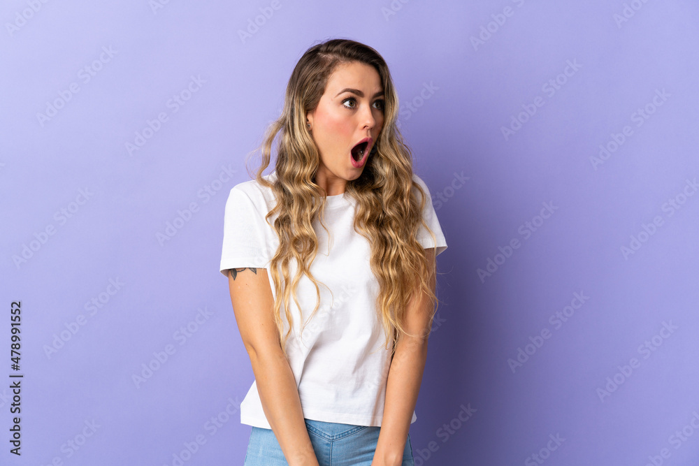 Young Brazilian woman isolated on purple background doing surprise gesture while looking to the side Young Brazilian woman isolated on purple background doing surprise gesture while looking to the side