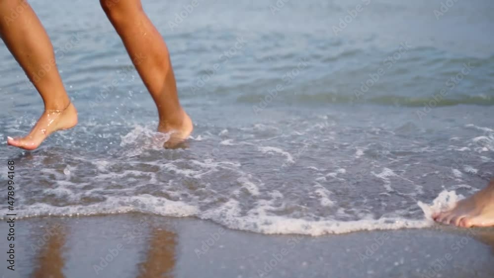 A couple is running, dancing along the surf line. Happy young people have fun on the sandy beach in summer. Slender tanned legs in the sea waves A couple is running, dancing along the surf line. Happy young people have fun on the sandy beach in summer. Slender tanned legs in the sea waves
