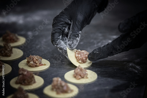 Hands in black gloves sculpt dumplings close-up, with shallow depth of field