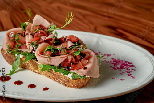 Bruschetta with tomato salsa and mortadella in a white plate on a wooden background