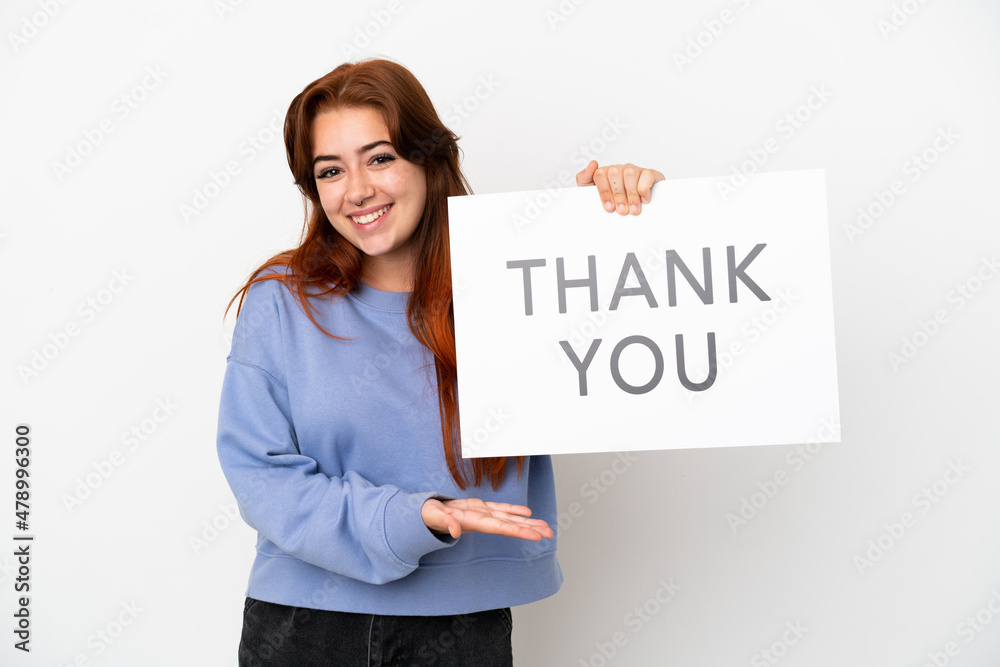 Young redhead woman isolated on white background holding a placard with text THANK YOU and pointing it Young redhead woman isolated on white background holding a placard with text THANK YOU and pointing it