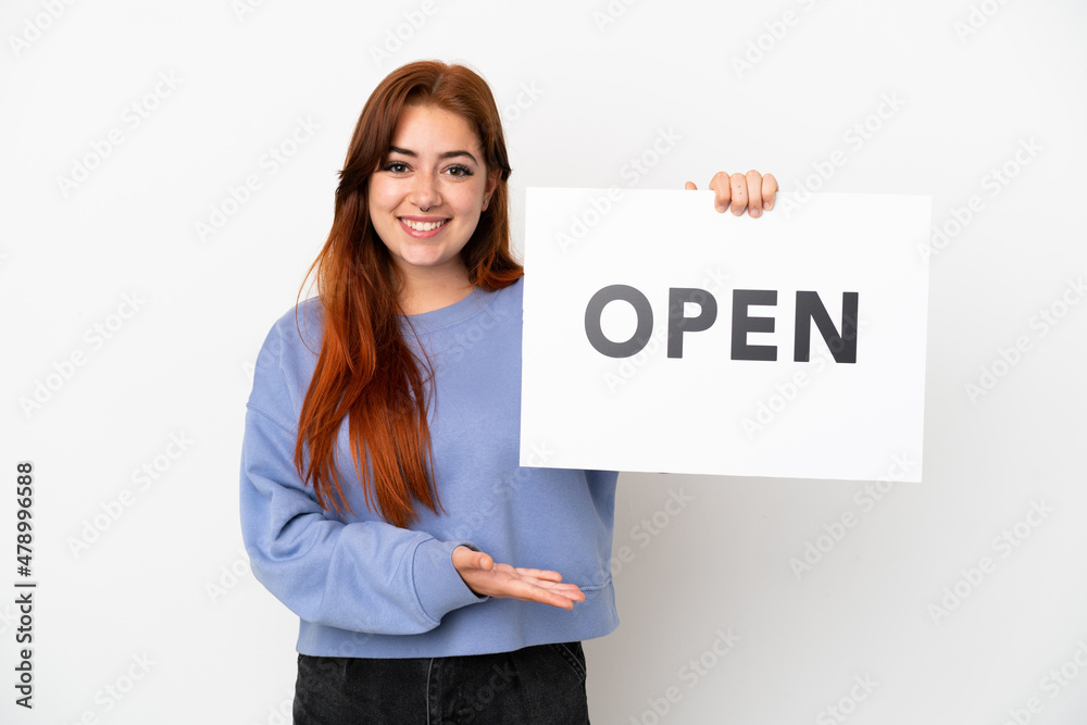 Young redhead woman isolated on white background holding a placard with text OPEN with happy expression Young redhead woman isolated on white background holding a placard with text OPEN with happy expression