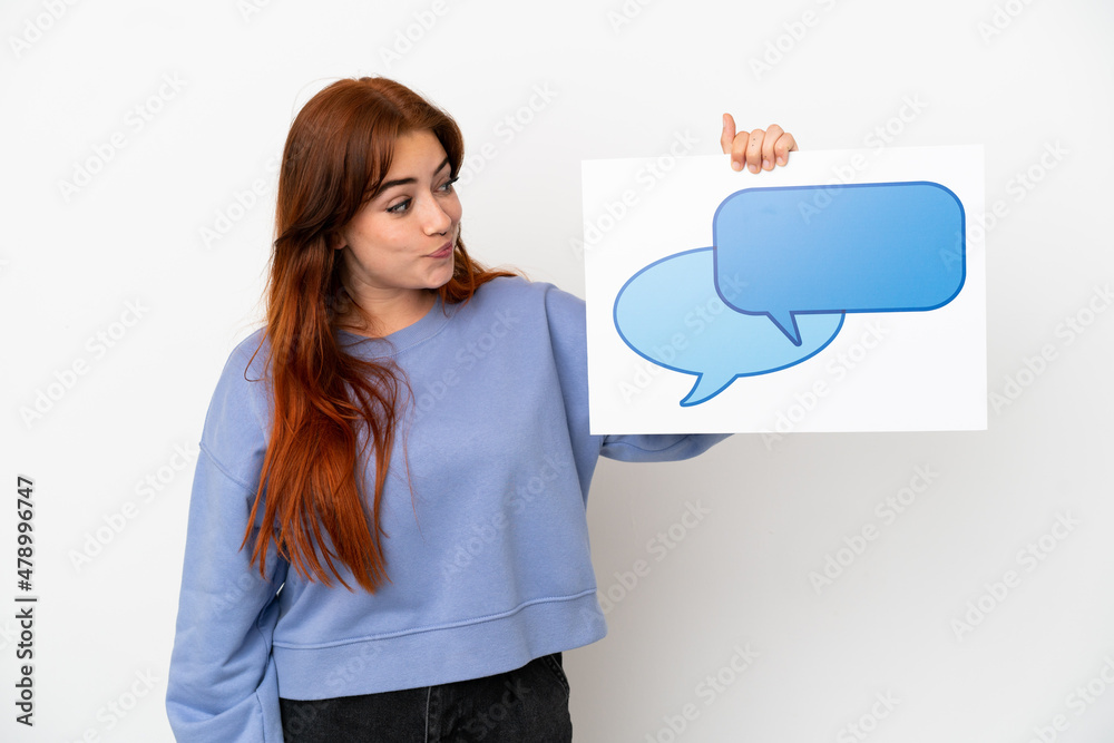 Young redhead woman isolated on white background holding a placard with speech bubble icon Young redhead woman isolated on white background holding a placard with speech bubble icon