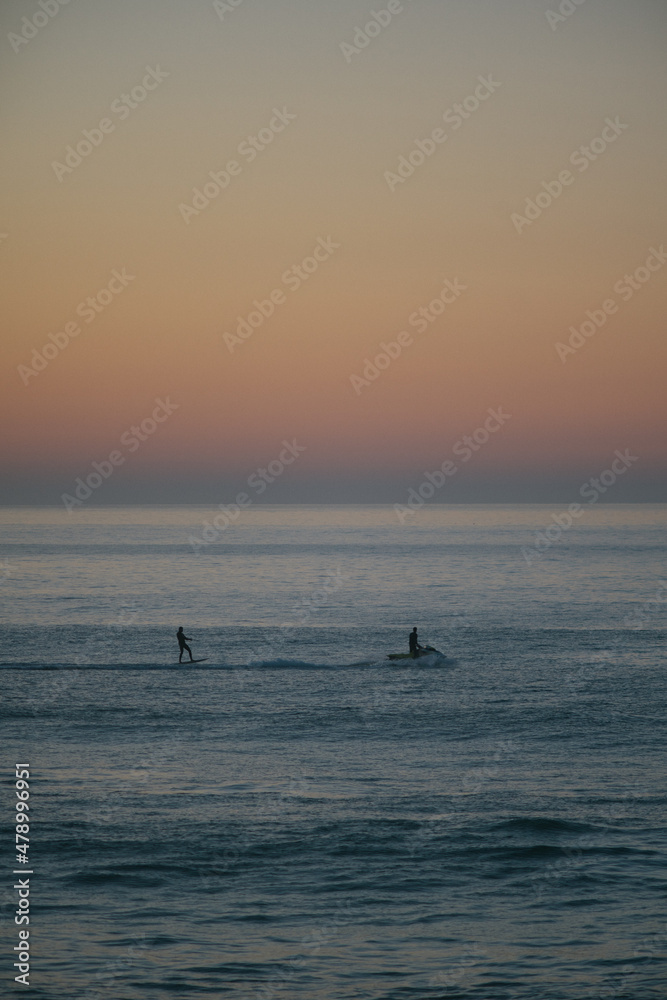 Jet ski towing a foil surfer during the sunset on atlantic ocean