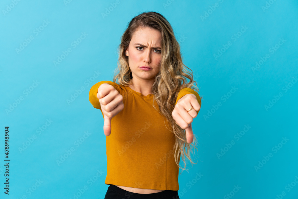 Young Brazilian woman isolated on blue background showing thumb down with two hands Young Brazilian woman isolated on blue background showing thumb down with two hands