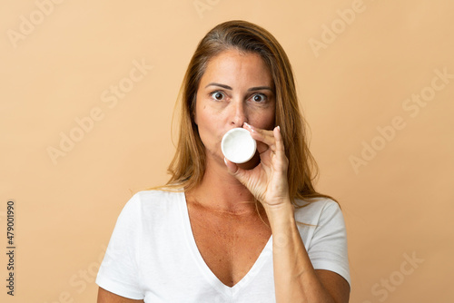 Middle age brazilian woman isolated on beige background with moisturizer