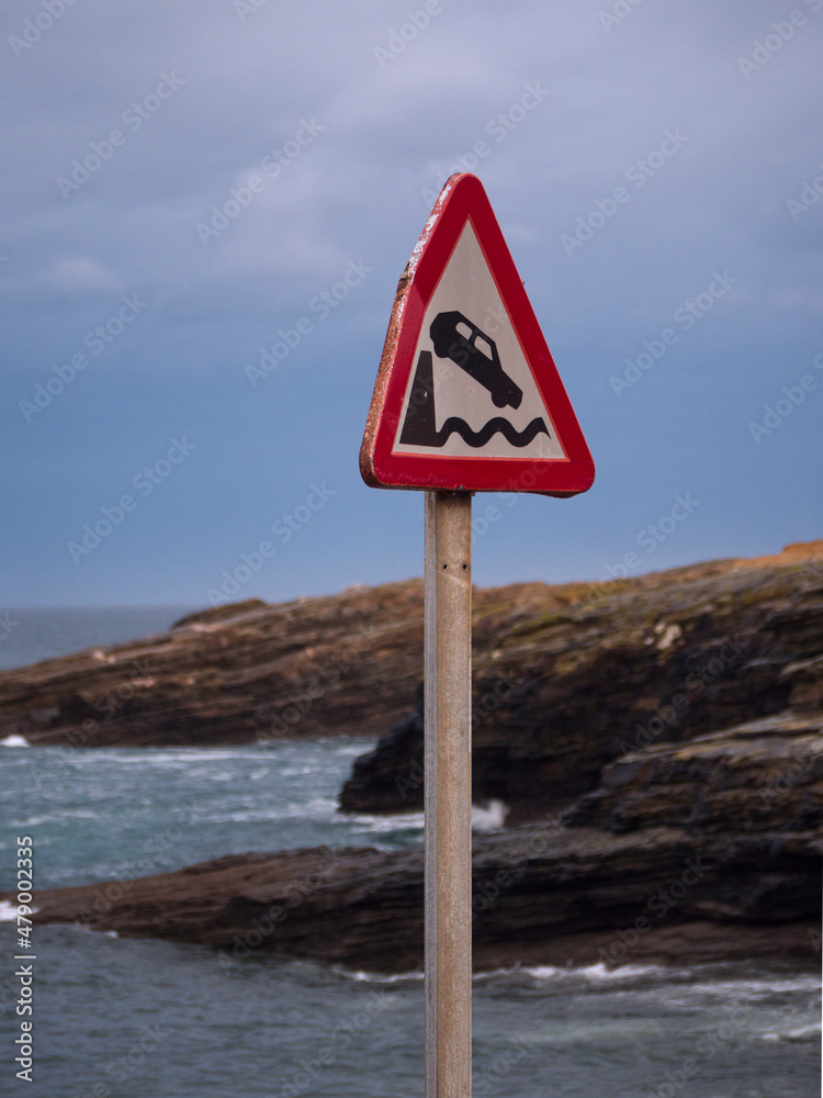 Warning traffic sign of end of road and fall into the sea and cloudy sky in the background.
