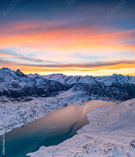 Aerial view of frozen lake Lago Bianco at Bernina mountain pass covered with snow at sunrise, Engadine, Graubunden, Switzerland