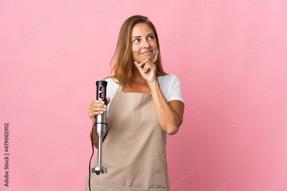 Middle age woman using hand blender isolated on pink background thinking an idea while looking up Middle age woman using hand blender isolated on pink background thinking an idea while looking up