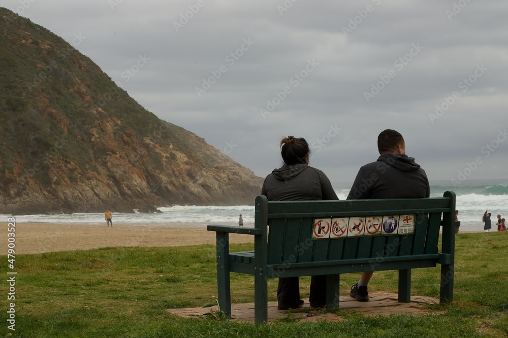 Two people sitting on a bench looking out accross a sea view at Herolds Bay in the Western Cape Province of South Africa.