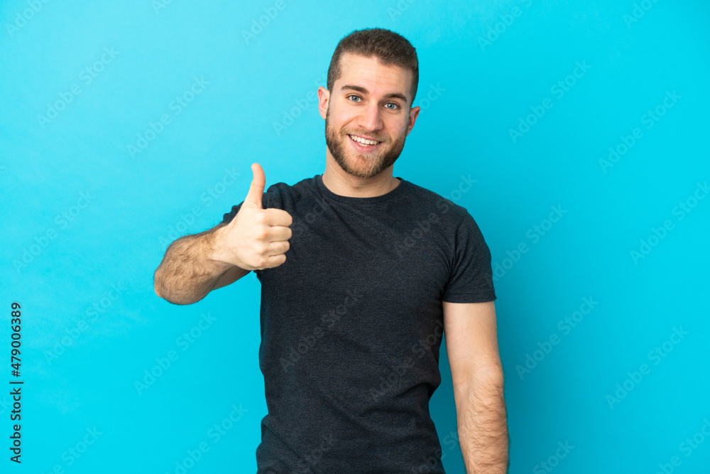 Young handsome caucasian man isolated on blue background with thumbs up because something good has happened Young handsome caucasian man isolated on blue background with thumbs up because something good has happened