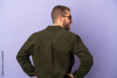 Young handsome caucasian man isolated on purple background in back position and looking side