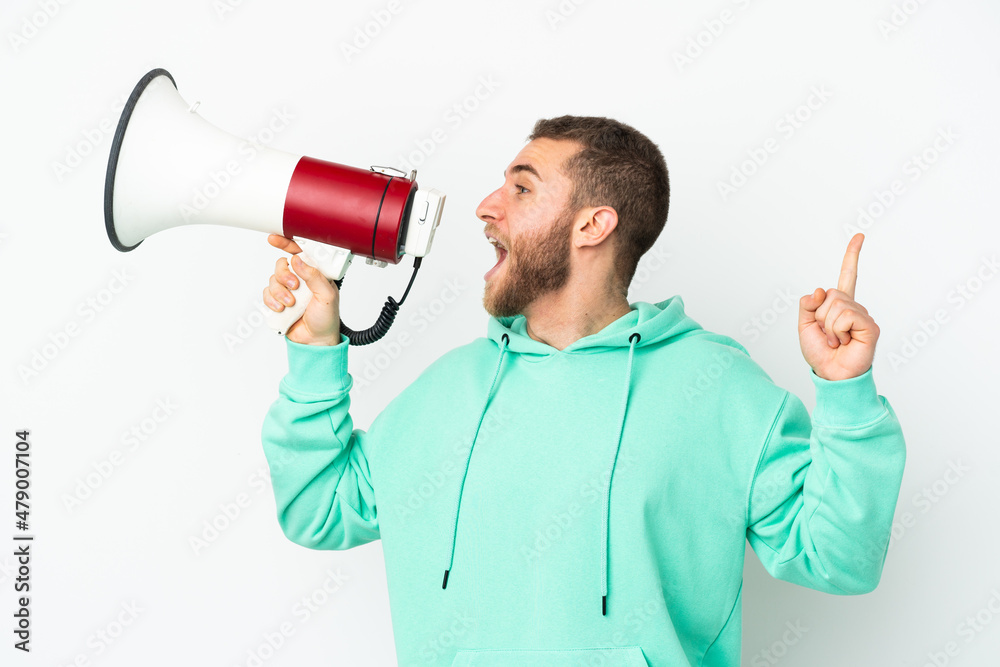 Young handsome caucasian man isolated on white background shouting through a megaphone to announce something in lateral position Young handsome caucasian man isolated on white background shouting through a megaphone to announce something in lateral position