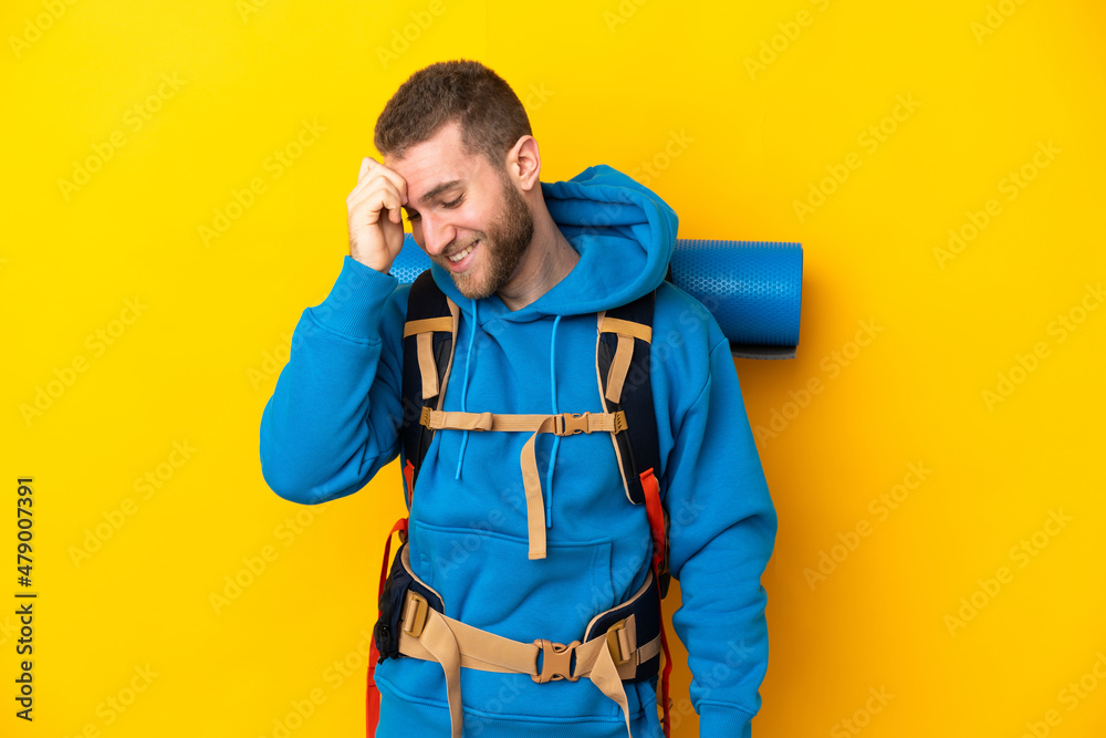 Young caucasian mountaineer man with a big backpack isolated on yellow background laughing Young caucasian mountaineer man with a big backpack isolated on yellow background laughing