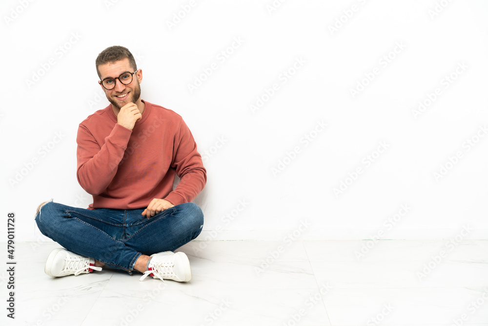 Young handsome man sitting on the floor with glasses and smiling Young handsome man sitting on the floor with glasses and smiling