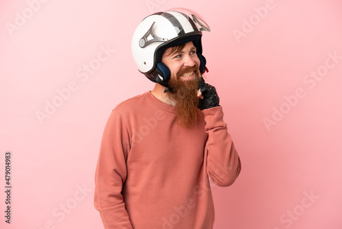 Young reddish caucasian man with a motorcycle helmet isolated on pink background thinking an idea while looking up