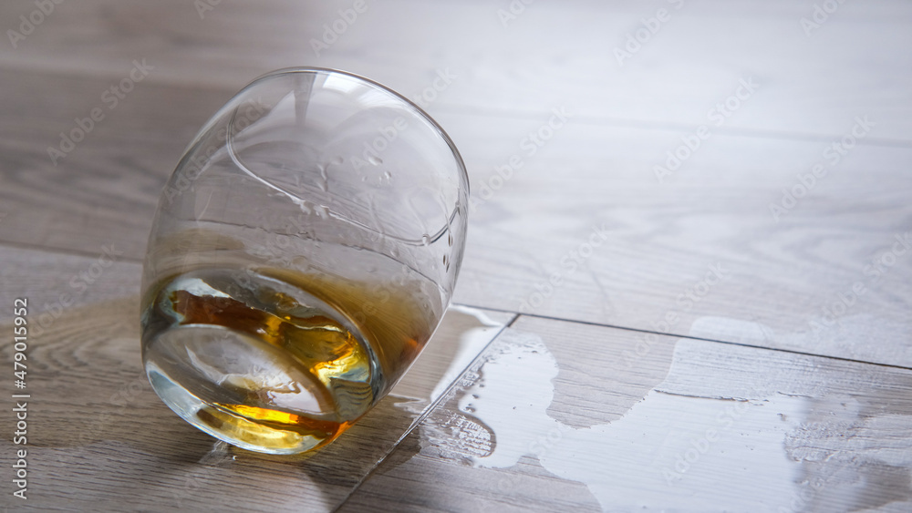 Spilled whiskey on the floor, there is an empty glass. Loneliness, alcoholism concept