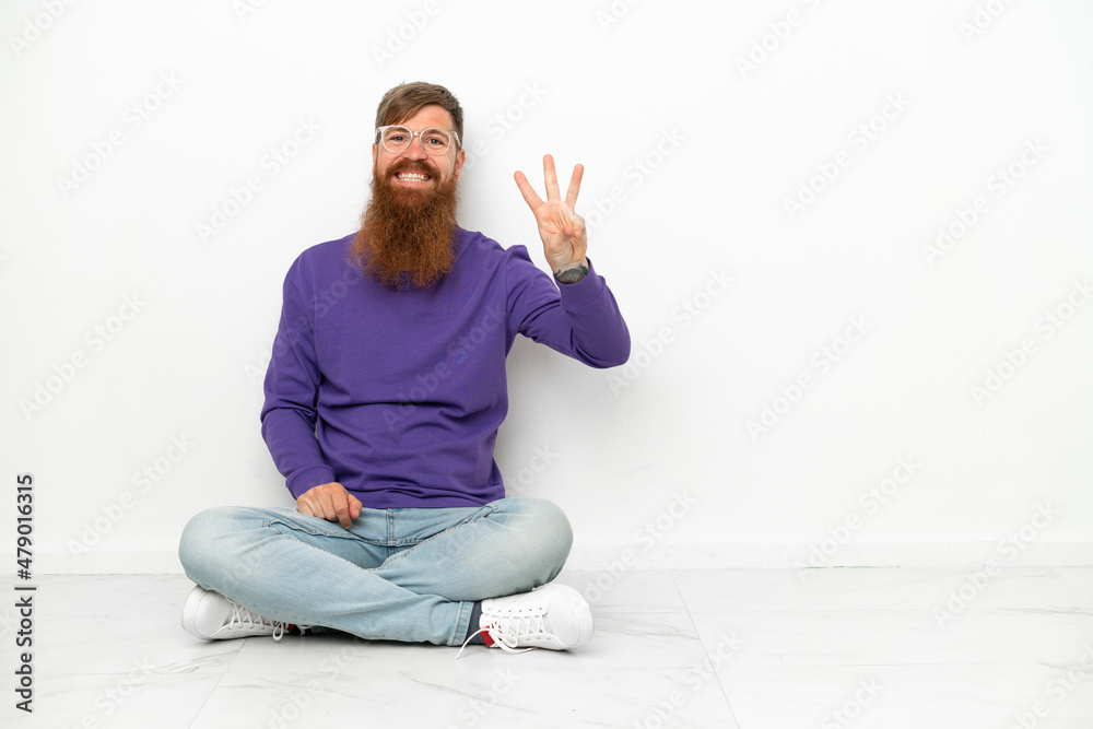 Young caucasian reddish man sitting on the floor isolated on white background happy and counting three with fingers Young caucasian reddish man sitting on the floor isolated on white background happy and counting three with fingers