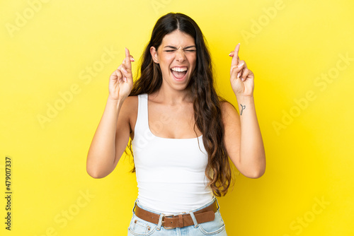 Young caucasian woman isolated on yellow background with fingers crossing